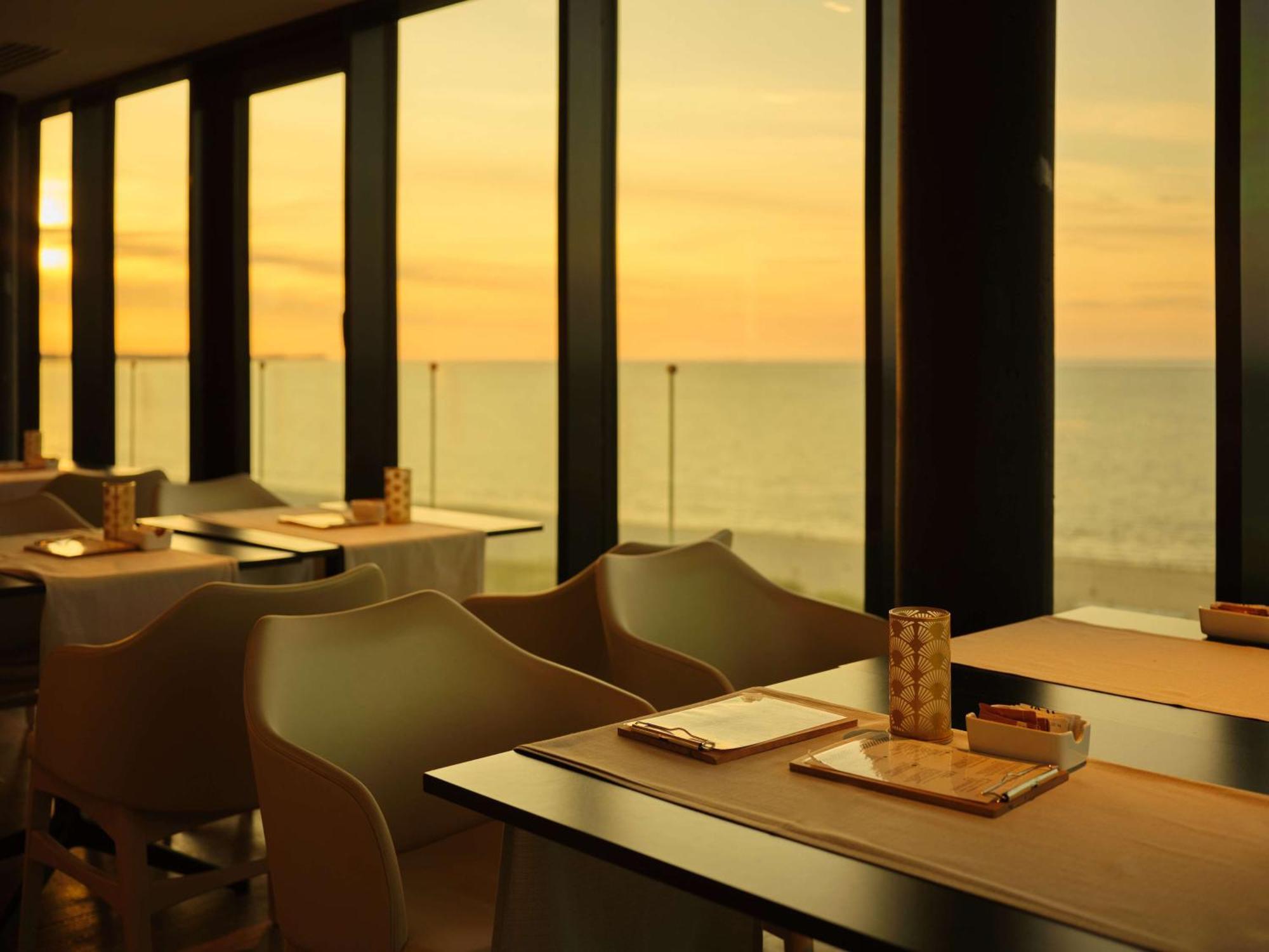 斯维诺乌伊希切丽笙布鲁酒店 外观 照片 The photo shows a restaurant interior with a beautiful view of the ocean during sunset. The large windows allow natural light to flood the space, highlighting the warm colors of the sunset in the sky. There are several tables, each set with placemats