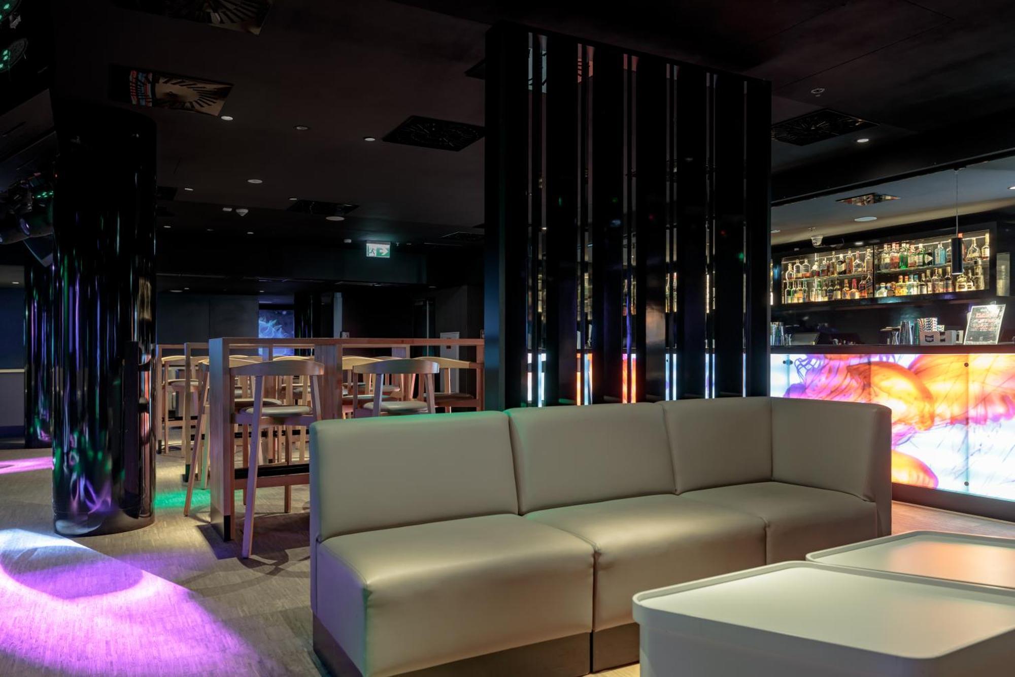 斯维诺乌伊希切丽笙布鲁酒店 外观 照片 The photo shows the interior of a stylish lounge or bar. The space features a modern design with dark walls and a sleek atmosphere. There is a beige sectional sofa in the foreground, providing a casual seating area. In the background, a bar is visibl