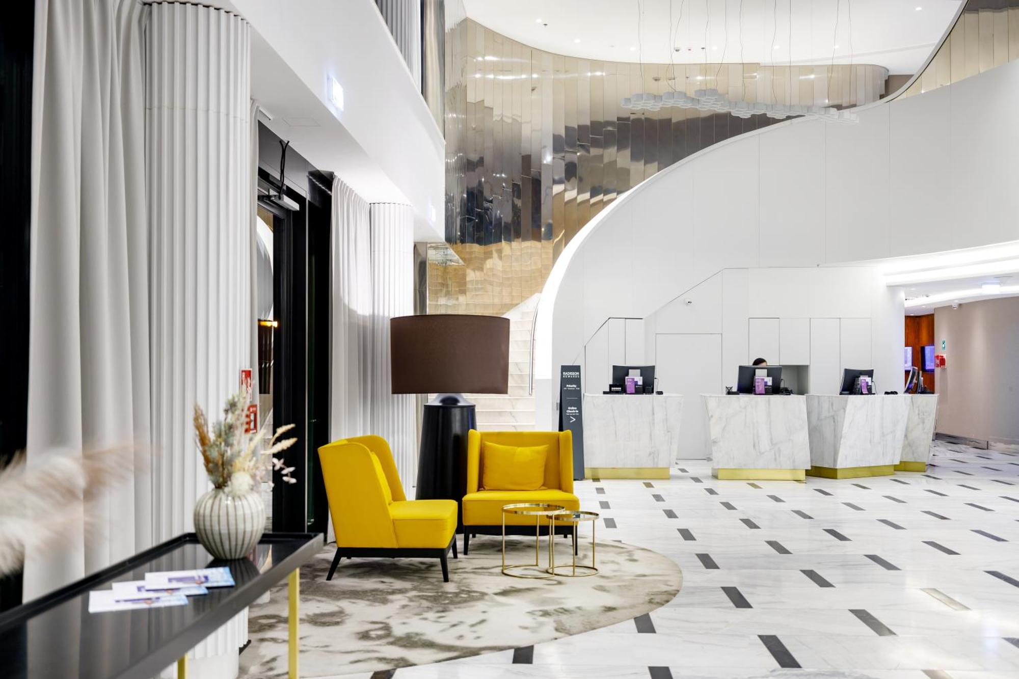 斯维诺乌伊希切丽笙布鲁酒店 外观 照片 The photo shows the interior of a modern hotel lobby. The space features a stylish design with a combination of yellow and neutral-colored seating, including two yellow armchairs and a small table. In the background, there is a reception area with ma