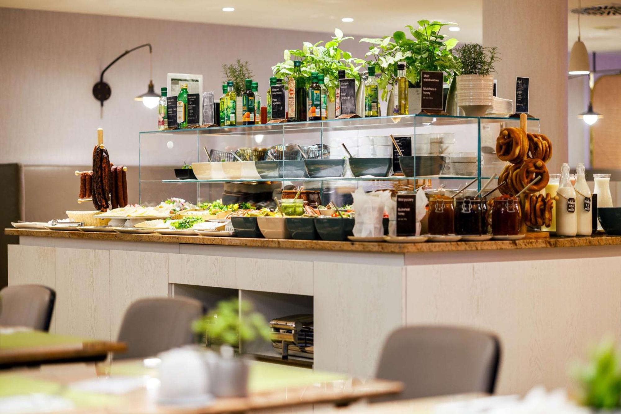 斯维诺乌伊希切丽笙布鲁酒店 外观 照片 The photo shows a well-organized buffet display in a restaurant setting. There is a glass counter filled with various dishes. On the upper shelf, there are several bottles of oil and herbs, indicating a focus on fresh and healthy ingredients. Below t