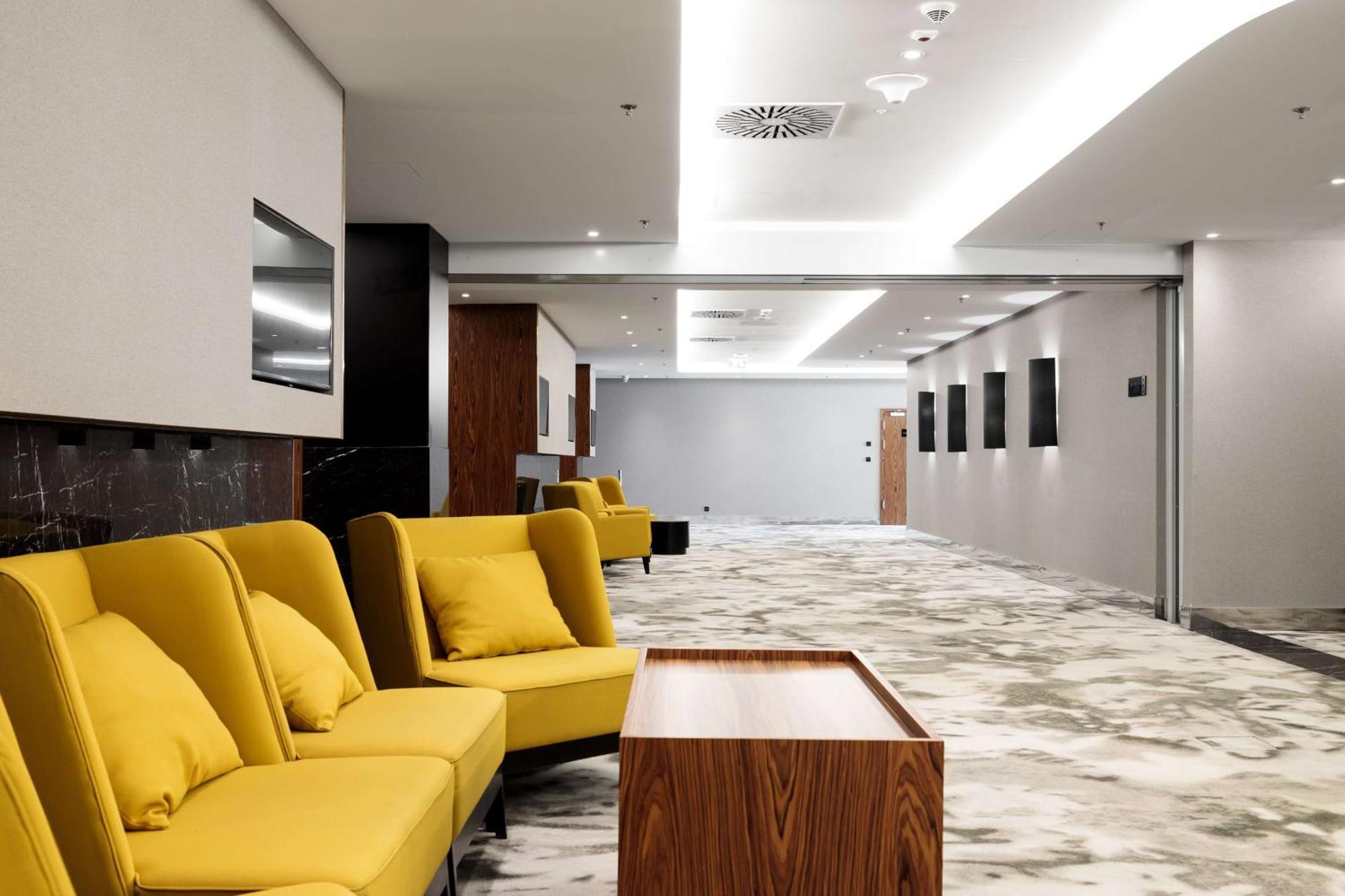 斯维诺乌伊希切丽笙布鲁酒店 外观 照片 The photo shows a modern interior space, likely a lobby or waiting area. There are several yellow sofas with cushions arranged in a casual seating area. In front of the sofas, there is a wooden coffee table. The flooring features a gray and white mar