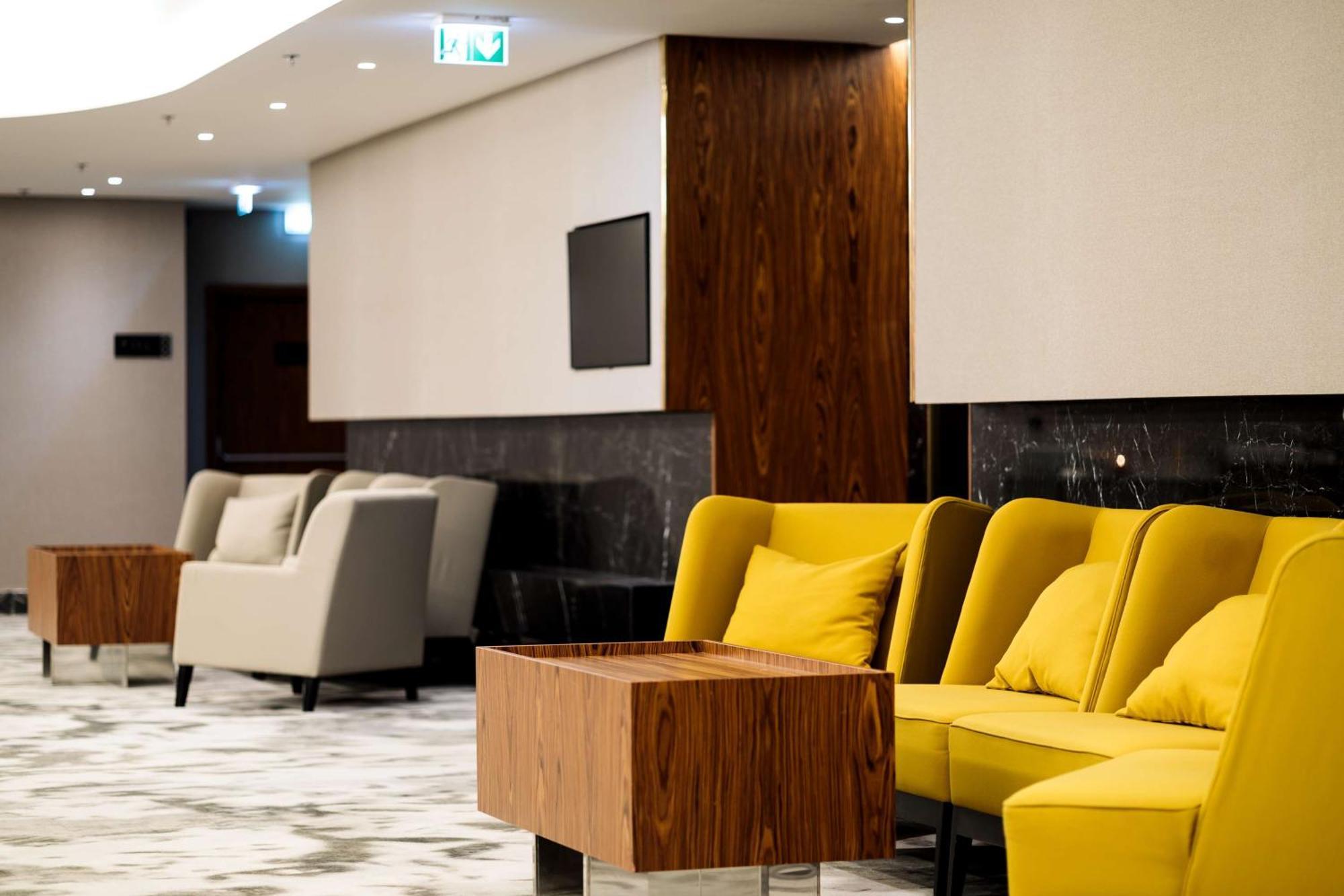 斯维诺乌伊希切丽笙布鲁酒店 外观 照片 The photo depicts a modern lounge or waiting area with stylish seating. On the left, there are soft gray armchairs arranged around a wooden coffee table. In the center, there are yellow chairs with plush cushions, contributing a vibrant contrast to t