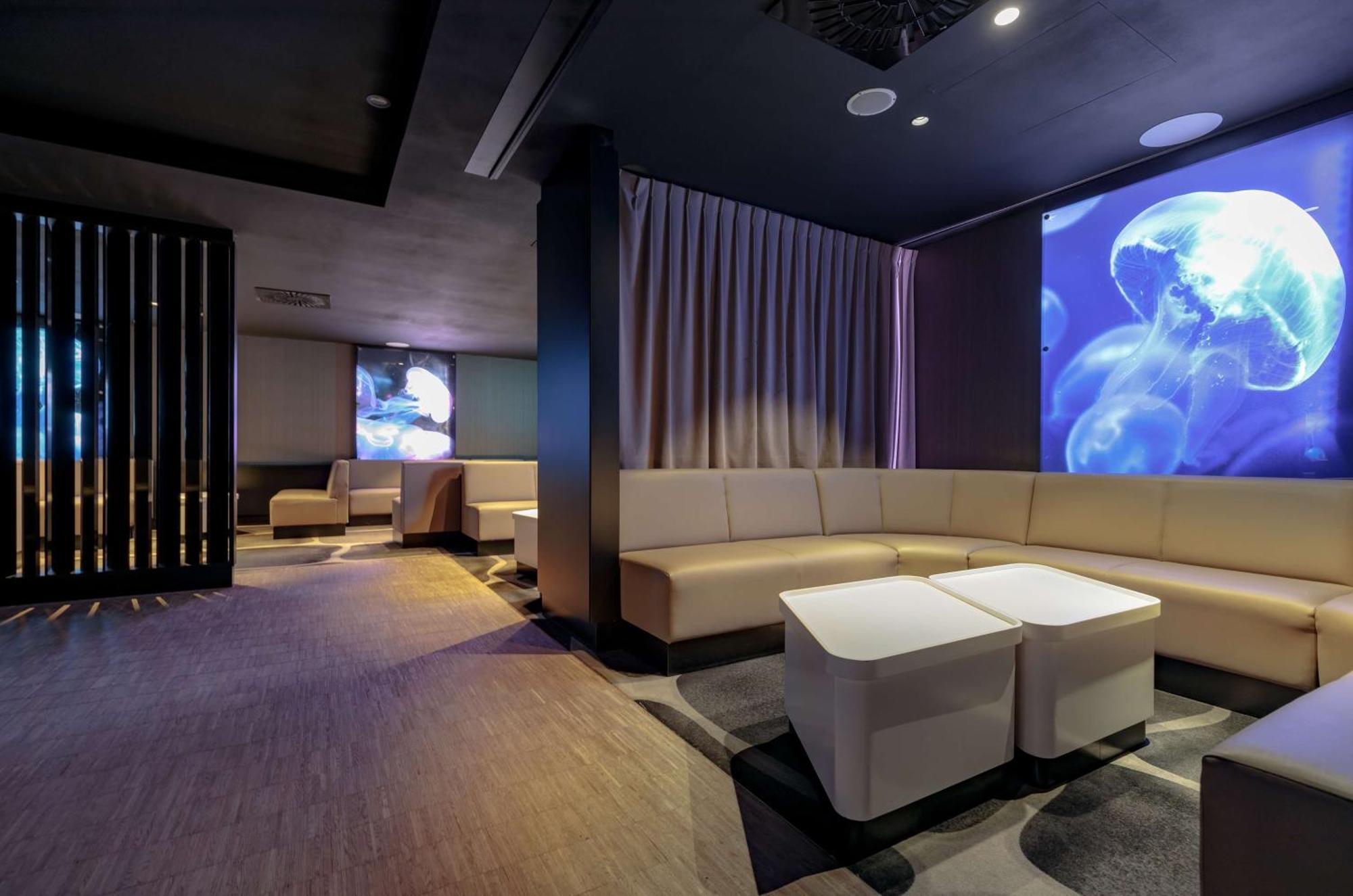 斯维诺乌伊希切丽笙布鲁酒店 外观 照片 The photo shows a modern interior space that appears to be a lounge or relaxation area. The design is sleek and minimalist, featuring a curved, light-colored seating arrangement with low tables at the center. The walls are dark, contributing to a coz