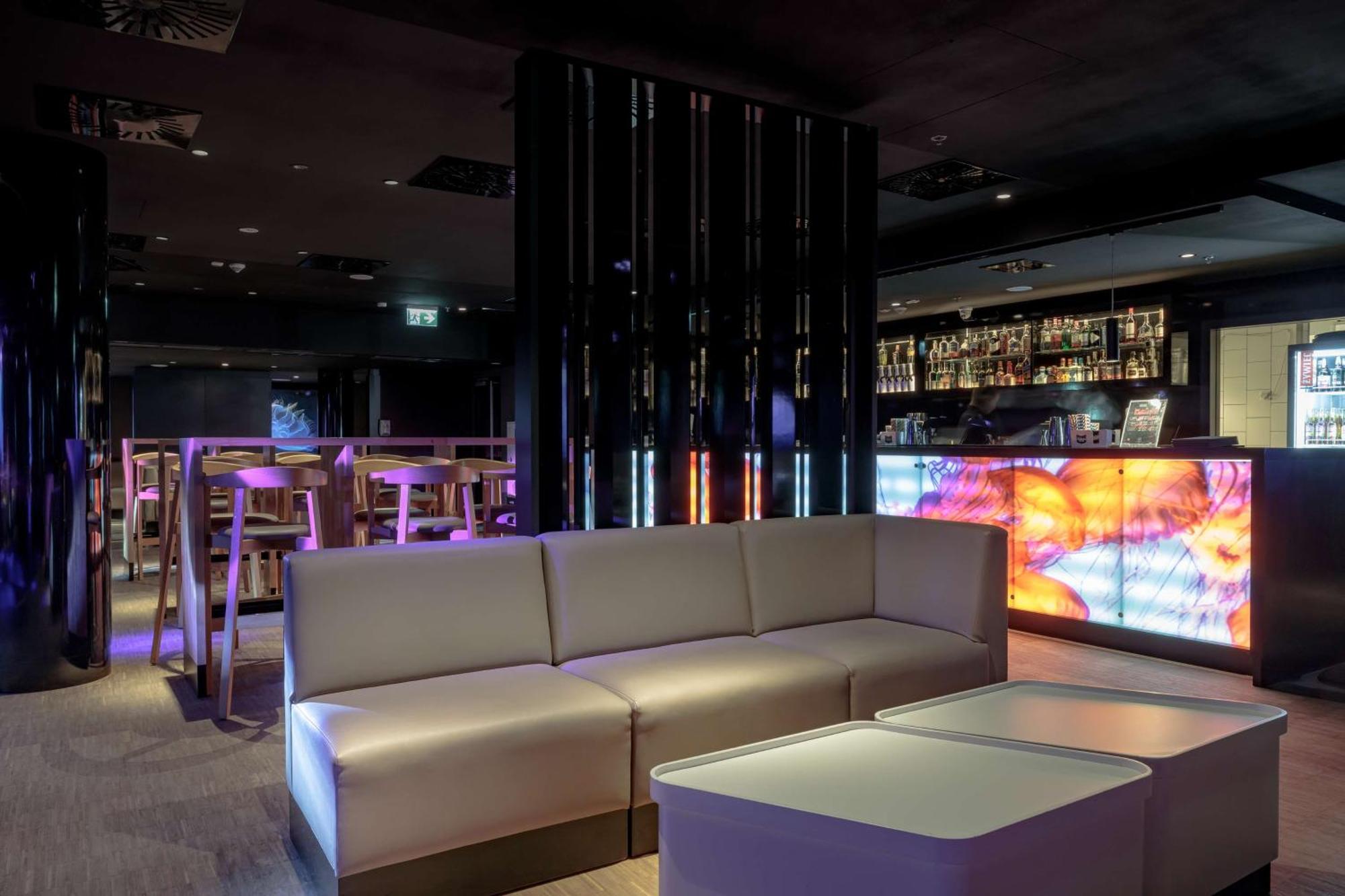 斯维诺乌伊希切丽笙布鲁酒店 外观 照片 The photo depicts a modern interior space, possibly a lounge or bar. There are sleek, minimalistic furniture pieces, including a large, curved sofa and contemporary coffee tables. The lighting is dim, with a blend of colorful ambient lights illuminat