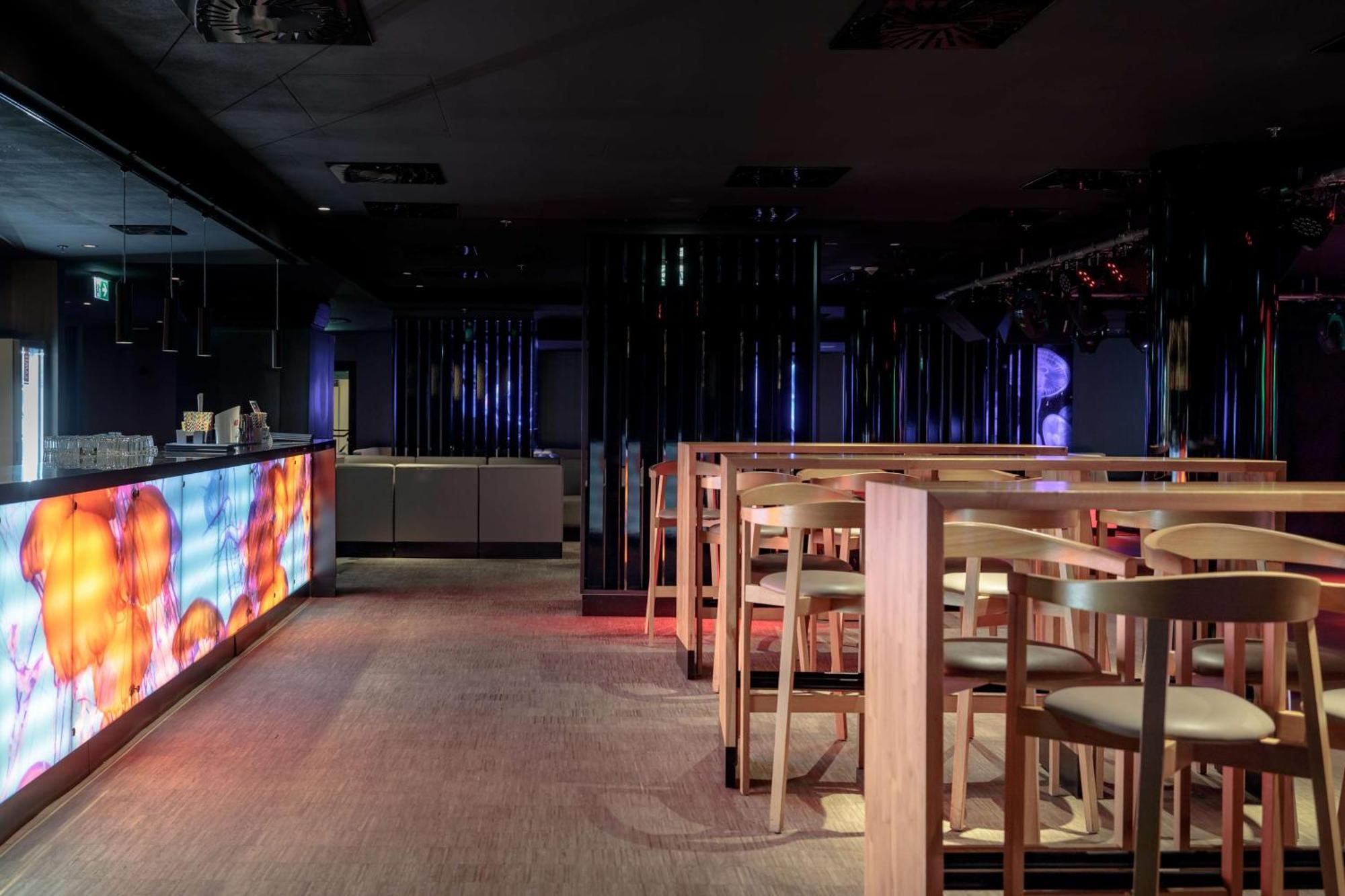 斯维诺乌伊希切丽笙布鲁酒店 外观 照片 The photo shows the interior of a modern bar or nightclub. It features a sleek and stylish design with a long bar counter illuminated by colorful lights. The floor has a neutral carpet, and there are wooden high-top tables with accompanying chairs ar