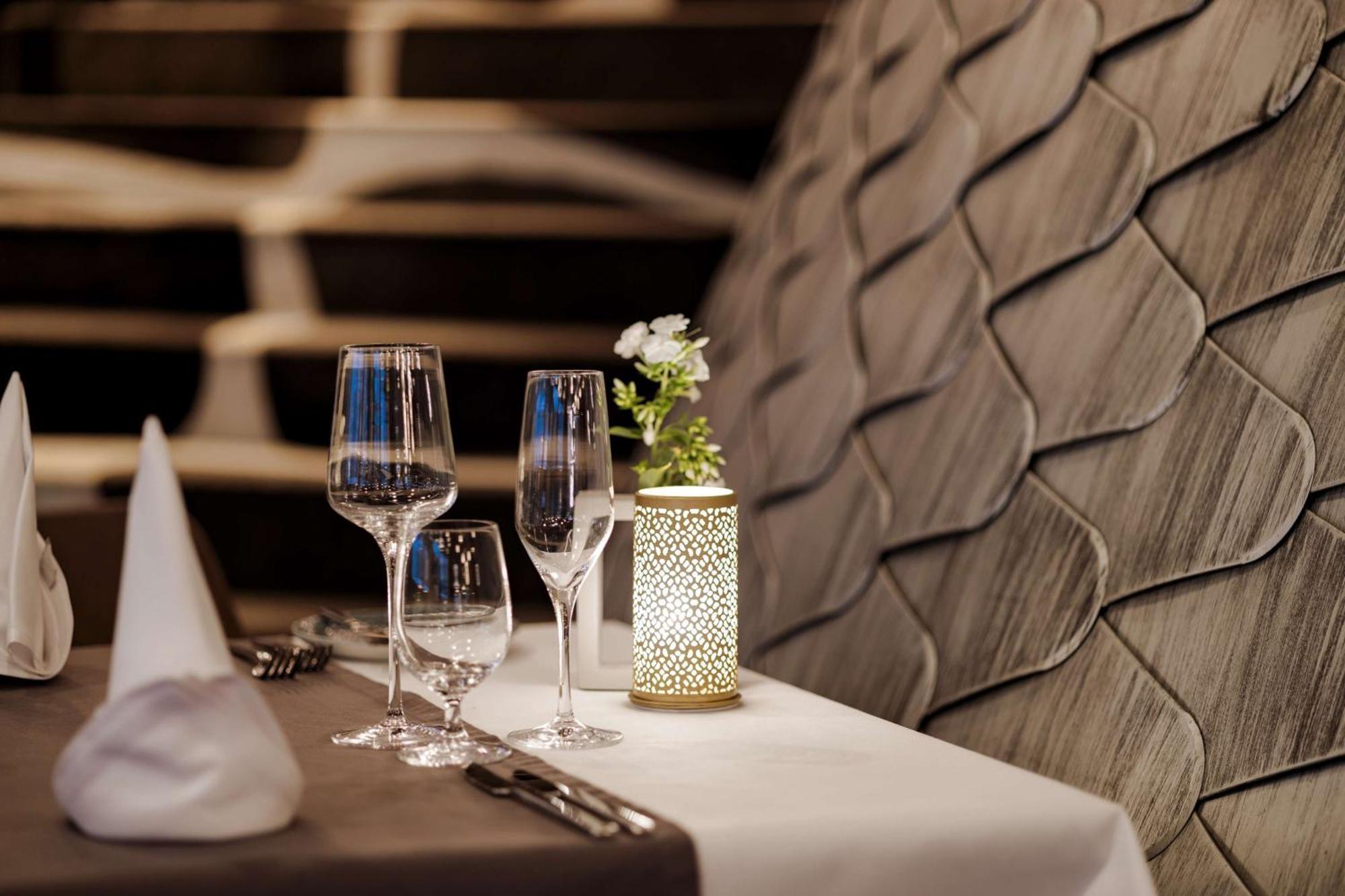 斯维诺乌伊希切丽笙布鲁酒店 外观 照片 The photo shows a beautifully arranged table setting in a restaurant. There are two elegant wine glasses and a smaller glass, likely for water, placed on a crisp white tablecloth. A decorative lantern with intricate designs holds a small flower arran