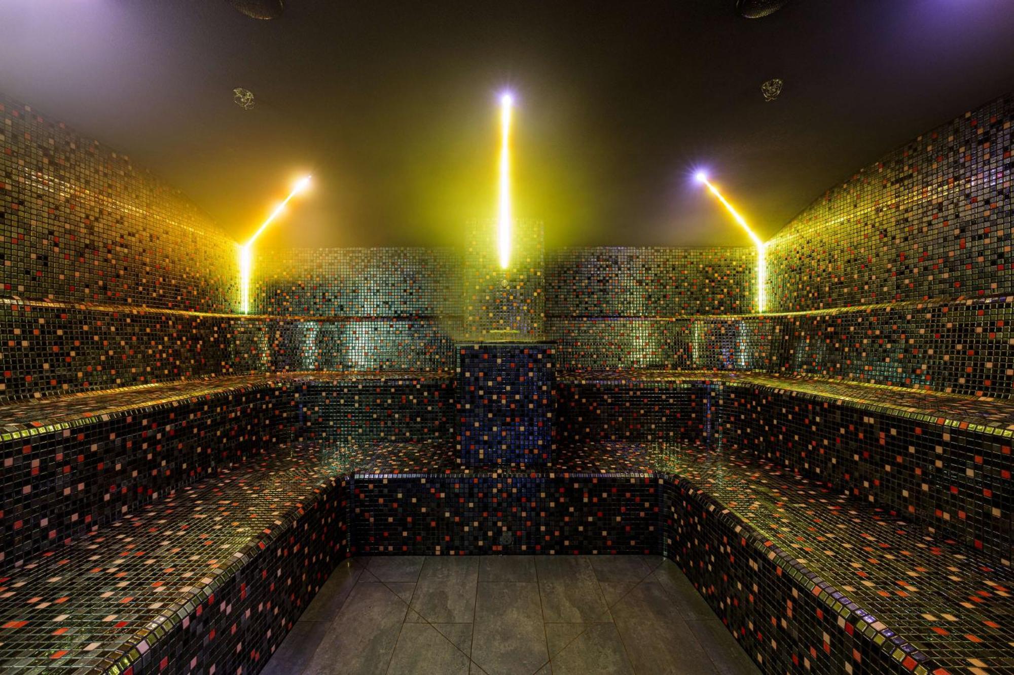 斯维诺乌伊希切丽笙布鲁酒店 外观 照片 The photo shows the interior of a steam room or sauna. The space is characterized by a series of benches that are built into the walls, allowing for multiple seating options. The walls are adorned with a mosaic of small, colorful tiles that create a 