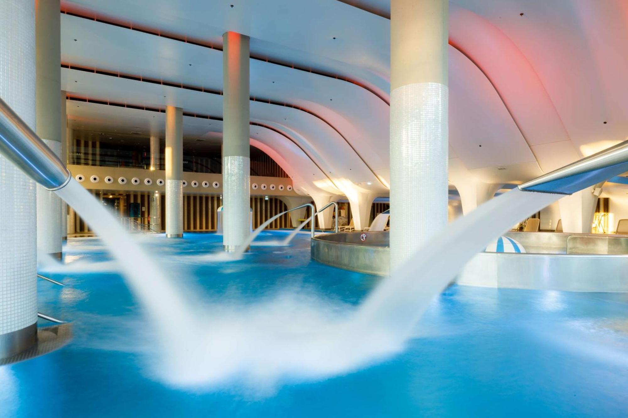 斯维诺乌伊希切丽笙布鲁酒店 外观 照片 The photo depicts an indoor swimming pool area characterized by modern architecture. The pool is filled with clear blue water, and there are several columns supporting the ceiling. Water features, such as jets or fountains, are seen creating flowing 